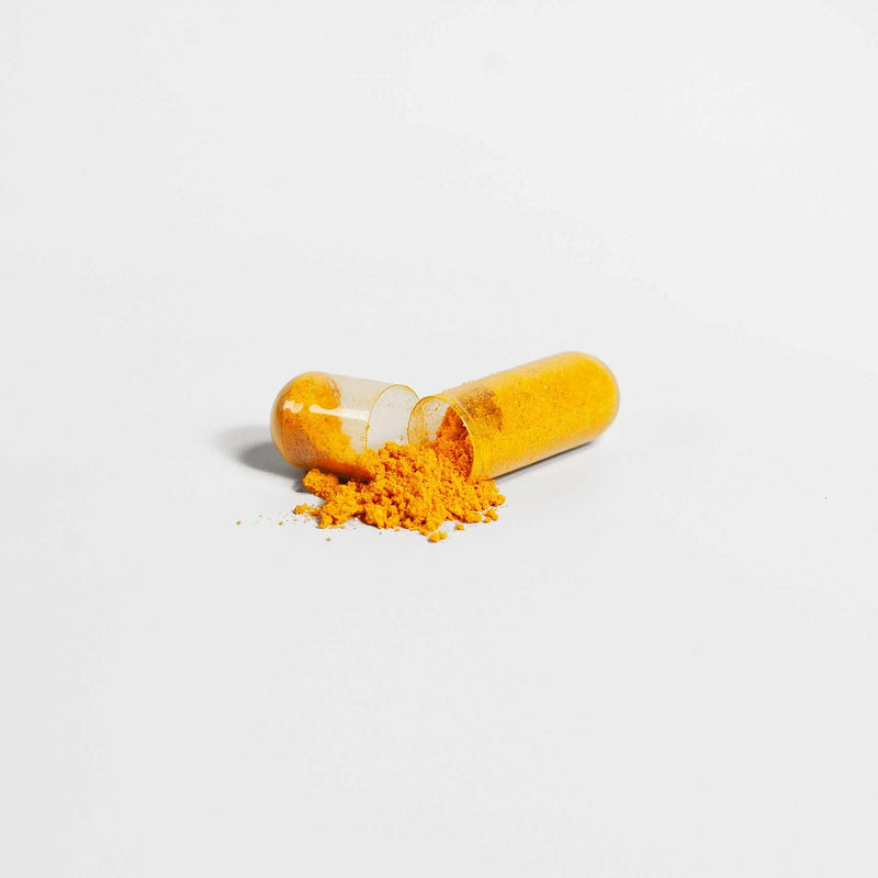 Open turmeric supplement capsule with turmeric powder on a white background.