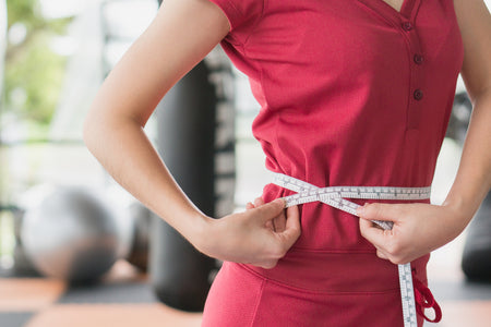 A person in fitness attire measuring their waist with a tape measure, symbolizing weight management and health.